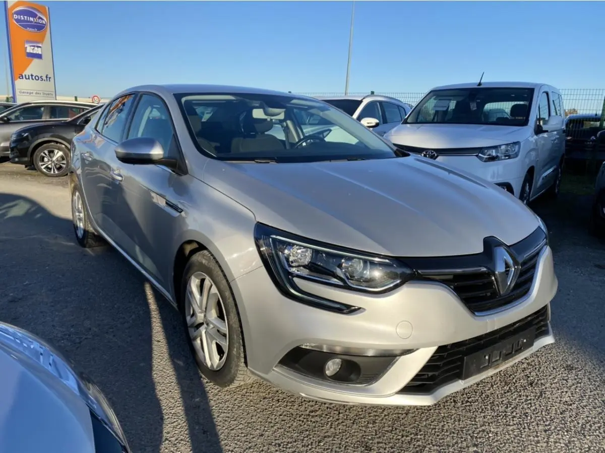 Renault Mégane Sedan gris platine vue 3/4 avant avec projecteurs antibrouillard et calandre noire brillante.