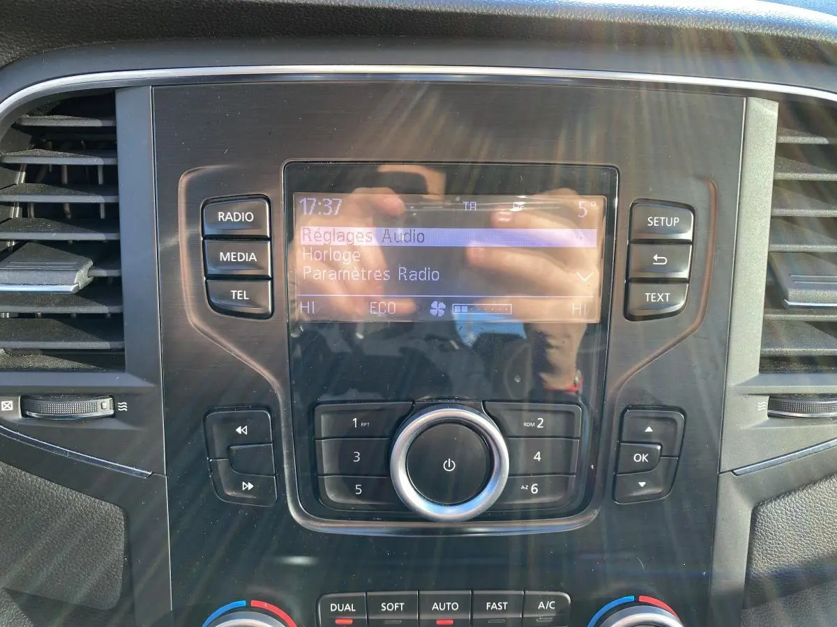 Gros plan sur la console centrale de la Renault Mégane gris platine, affichant l'écran radio et les commandes de climatisation.