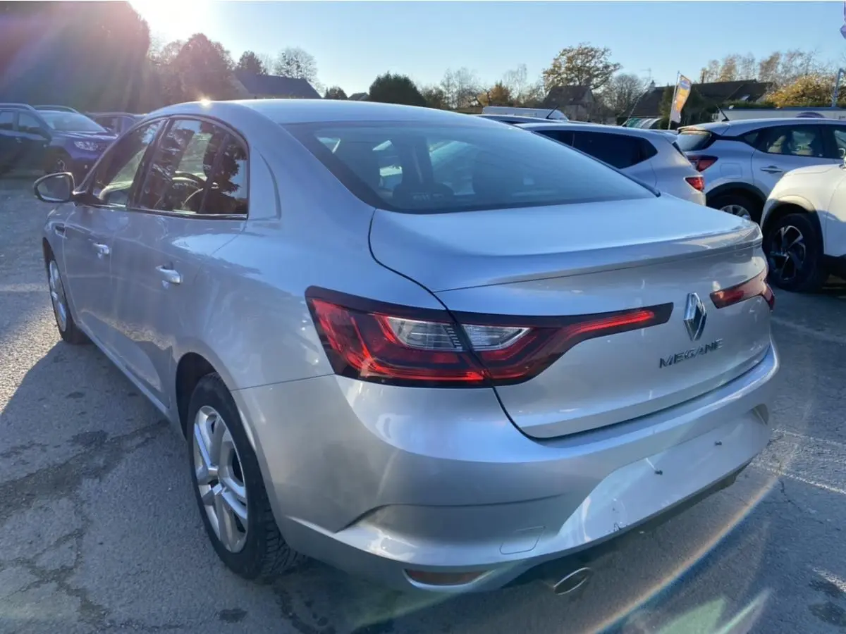 Vue 3/4 arrière droite d'une Renault Mégane Sedan gris platine avec feux arrière allongés et logo Renault visible.