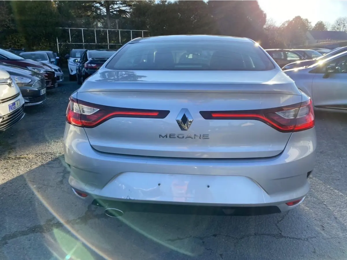 Vue arrière d'une Renault Mégane gris platine avec feux arrière allumés, stationnée en extérieur au soleil.