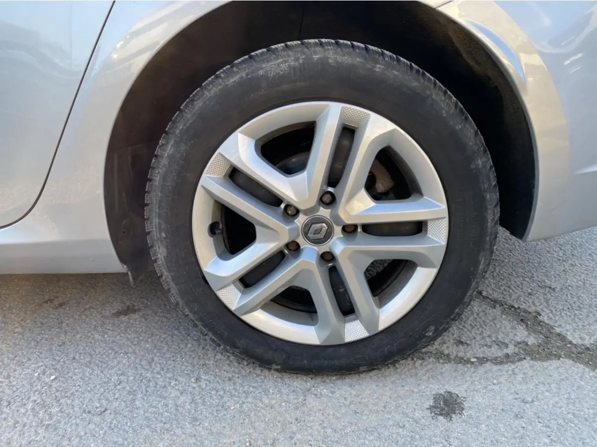 Gros plan sur la roue avant gauche d'une Renault Mégane gris platine, mettant en valeur la jante alliage au design moderne.