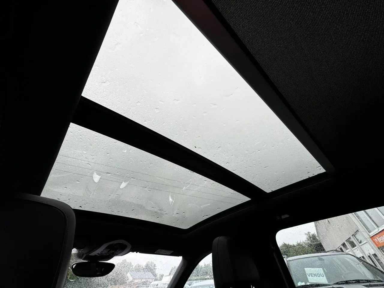 Toit ouvrant panoramique vu de l'intérieur du Porsche Cayenne noir, avec pluie visible sur le verre et sièges en cuir.