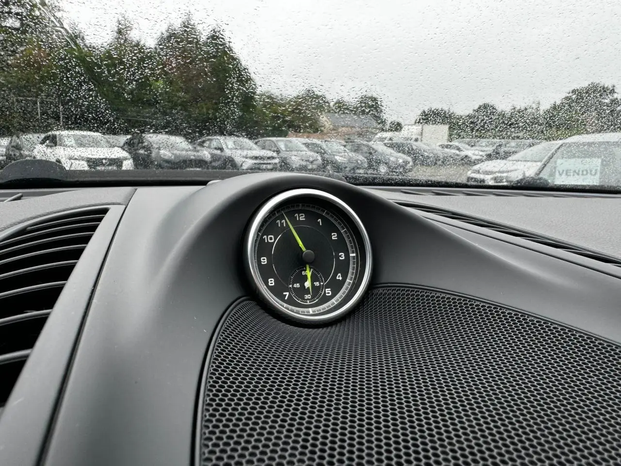 Gros plan sur le chronomètre analogique noir du tableau de bord d'un Porsche Cayenne noir, pluie visible à l'extérieur.