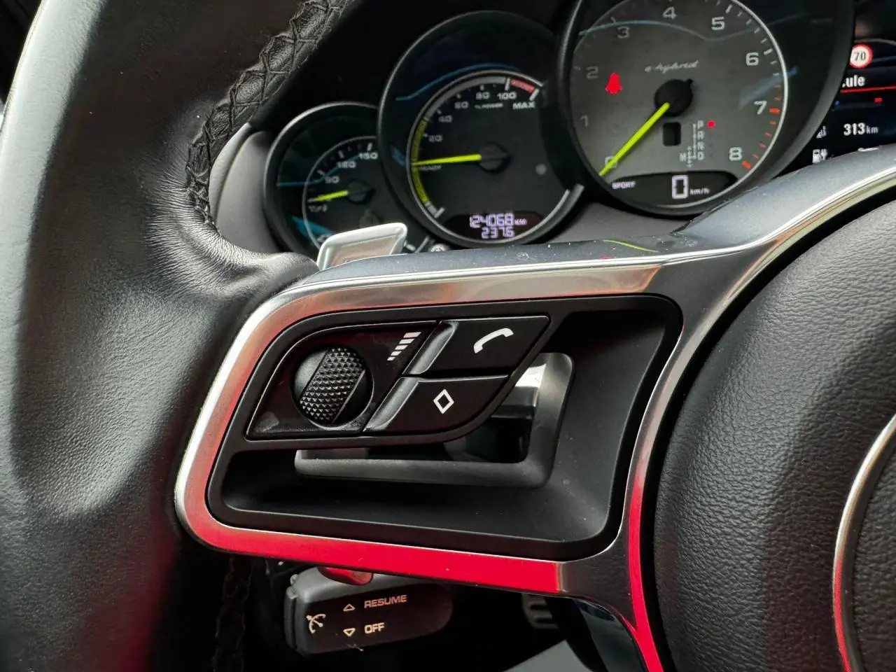 Gros plan sur la partie gauche du volant cuir du Porsche Cayenne 2017 avec commandes multifonctions et compte-tours e-hybrid.