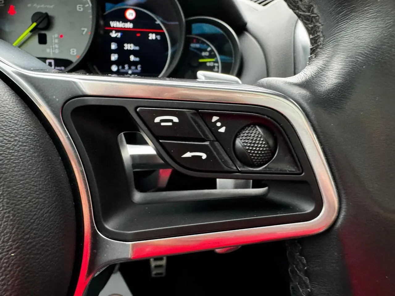 Gros plan sur les commandes du volant cuir noir du Porsche Cayenne S E-Hybrid 2017 avec affichage numérique en arrière-plan.