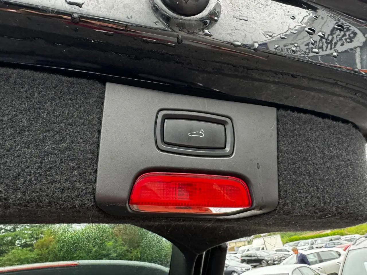 Gros plan sur le bouton d'ouverture du coffre et feu rouge sous le hayon noir du Porsche Cayenne S E-Hybrid 2017.