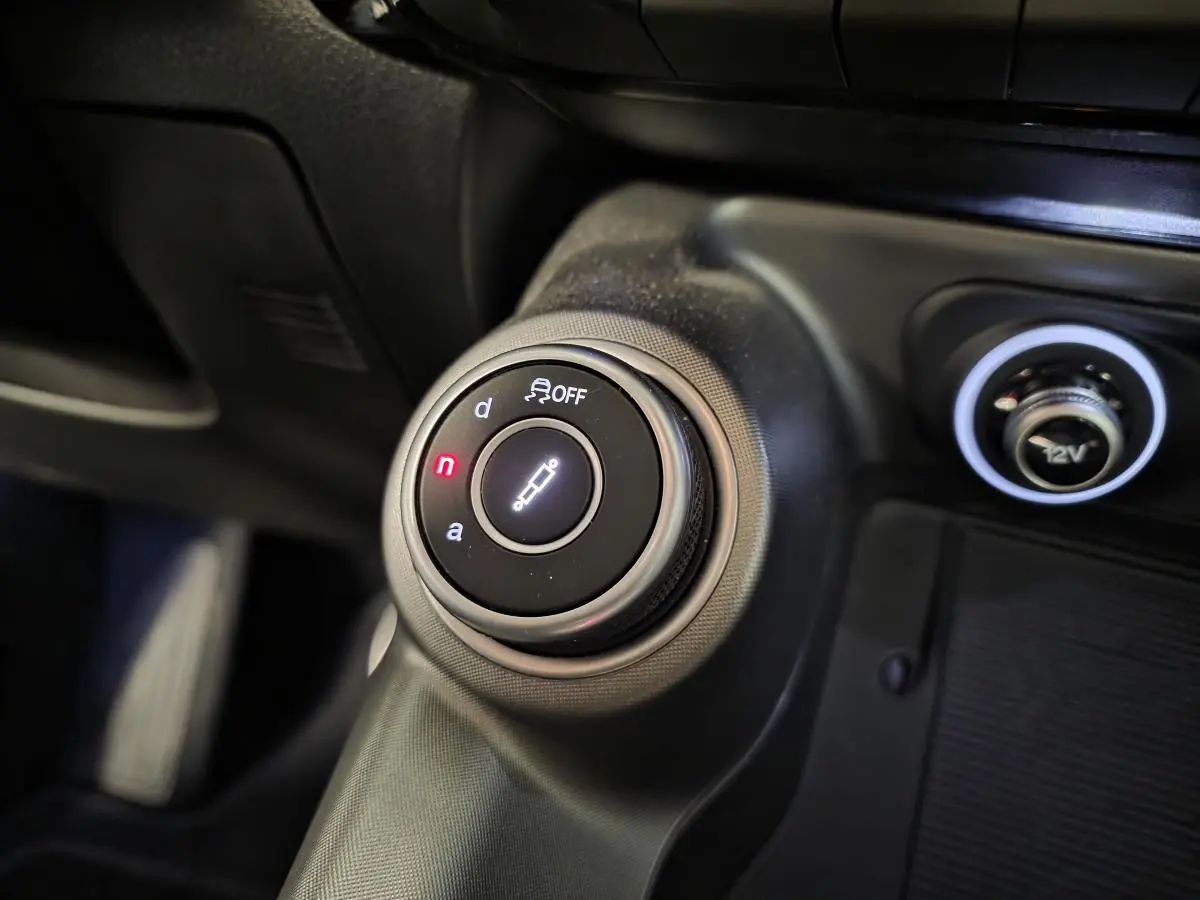 Gros plan sur le sélecteur de modes de conduite Alfa DNA et prise 12V dans l'habitacle noir de l'Alfa Romeo Tonale Vert.