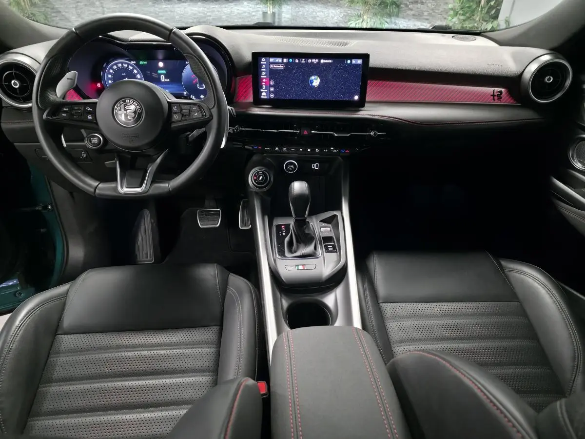 Vue intérieure centrée sur le tableau de bord et console d'une Alfa Romeo Tonale 2024, sellerie cuir noir et détails rouges.