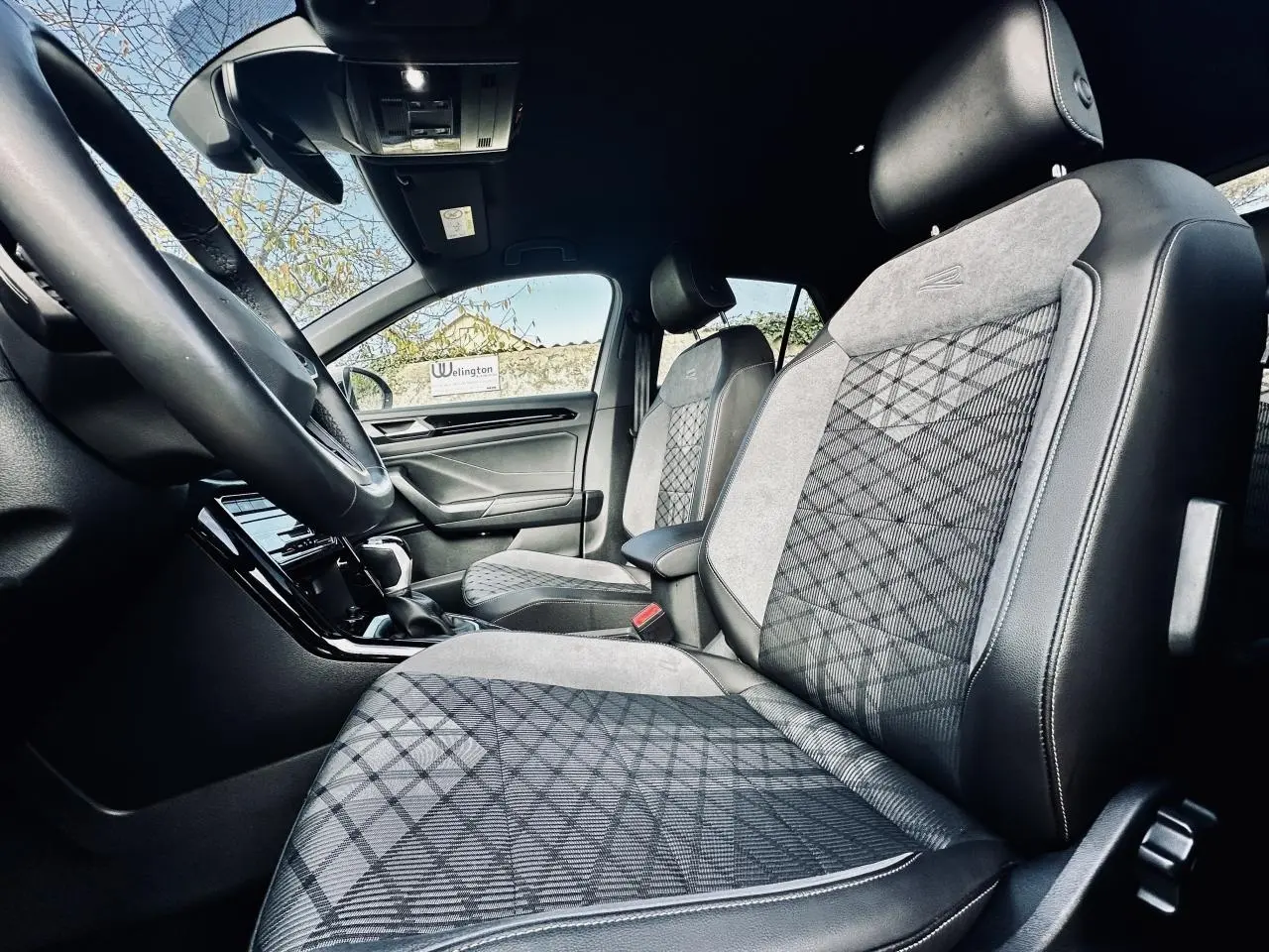 Vue intérieure côté conducteur du Volkswagen T-Roc 2024, sièges R-Line en tissu noir et gris avec motifs géométriques.