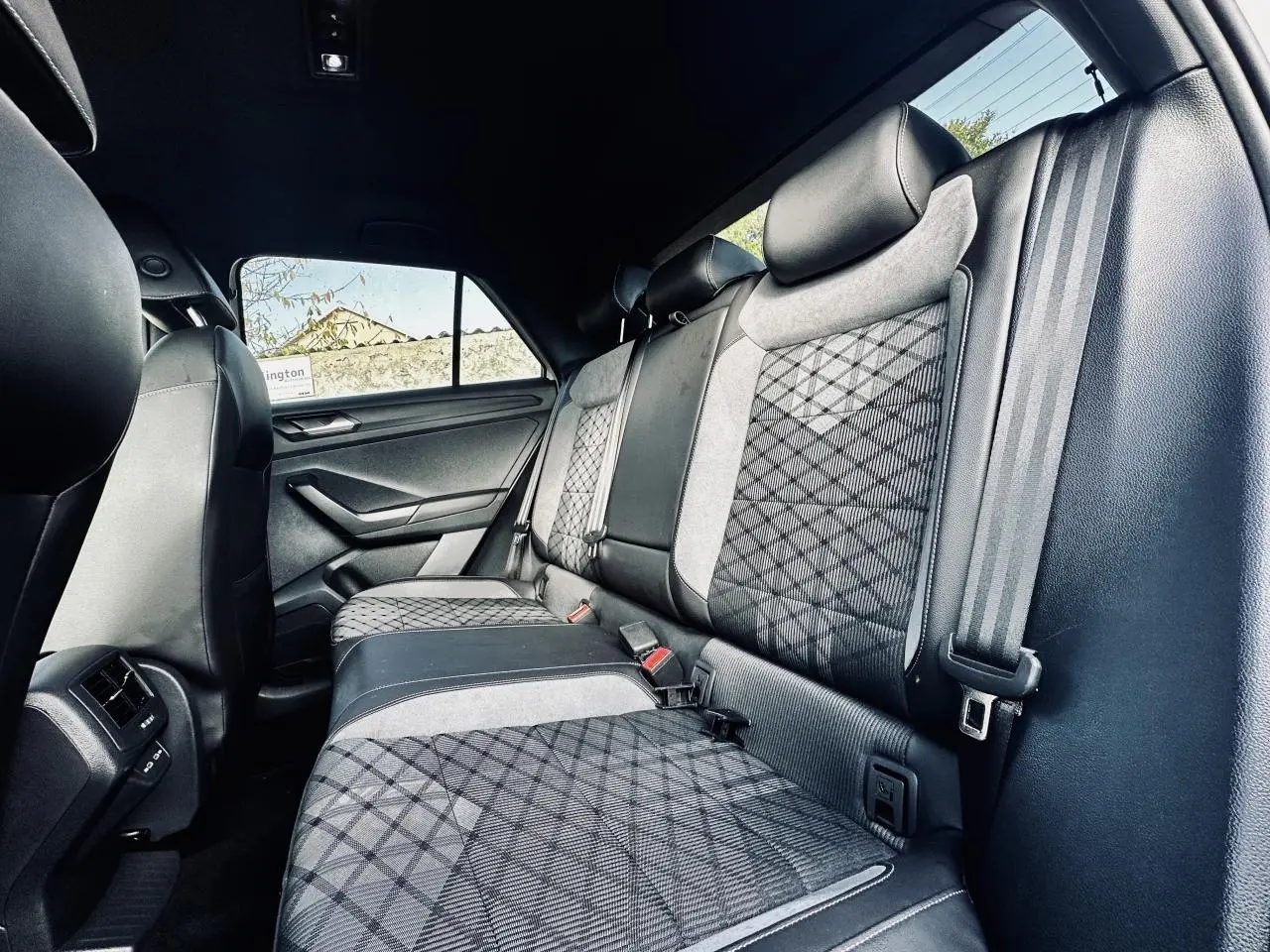 Vue intérieure arrière du Volkswagen T-Roc 2024, sièges arrière gris à motifs géométriques et ceintures de sécurité visibles.