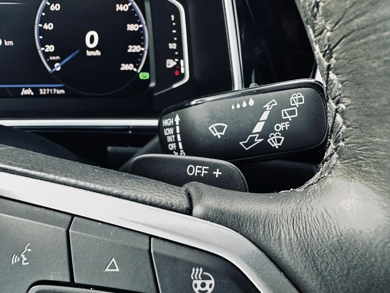 Gros plan sur le volant cuir noir et manette d'essuie-glace du Volkswagen T-Roc gris, tableau de bord digital en arrière-plan.