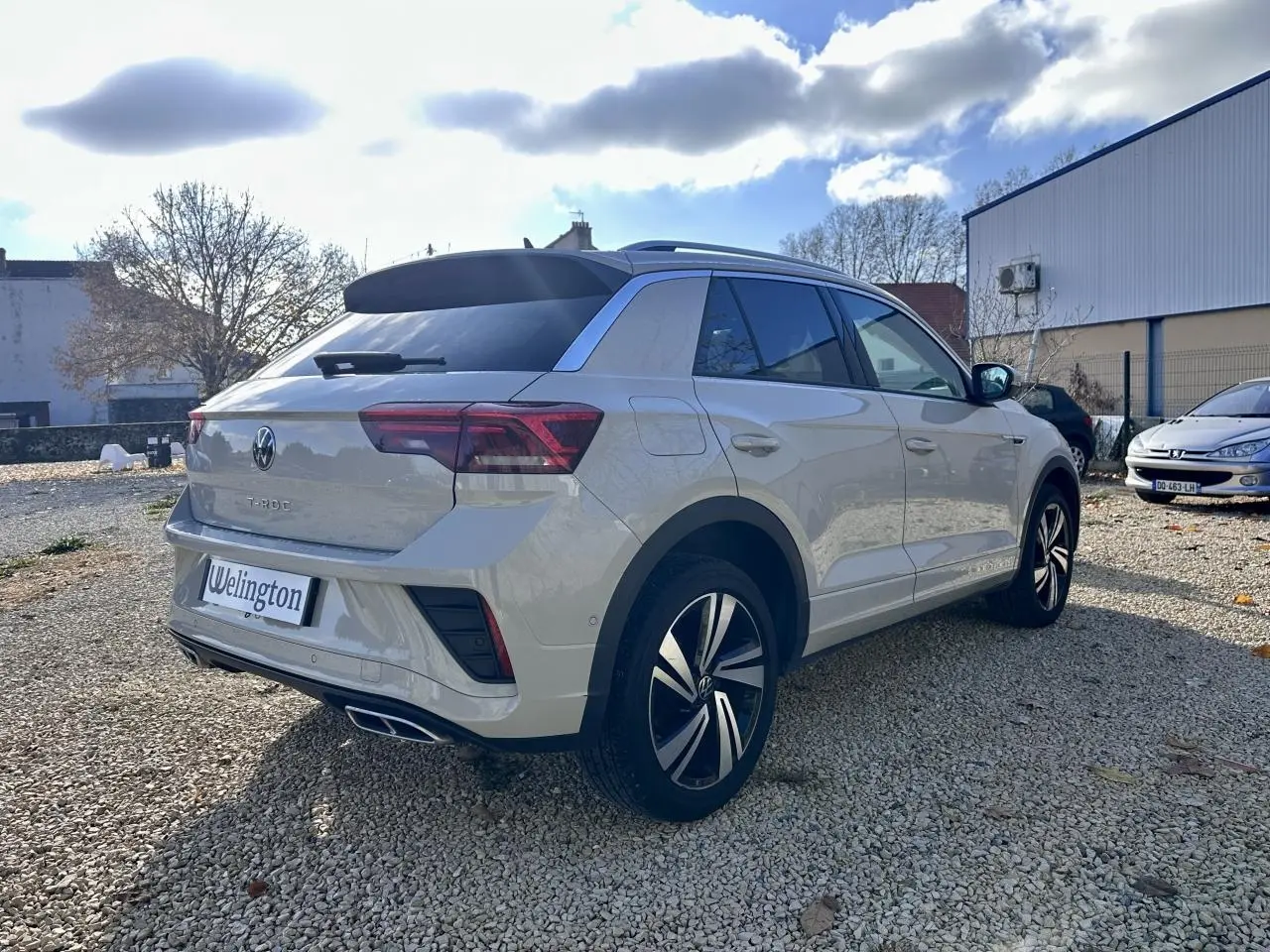 Volkswagen T-Roc gris vue 3/4 arrière droit sur parking, avec jantes alliage et toit noir contrasté.