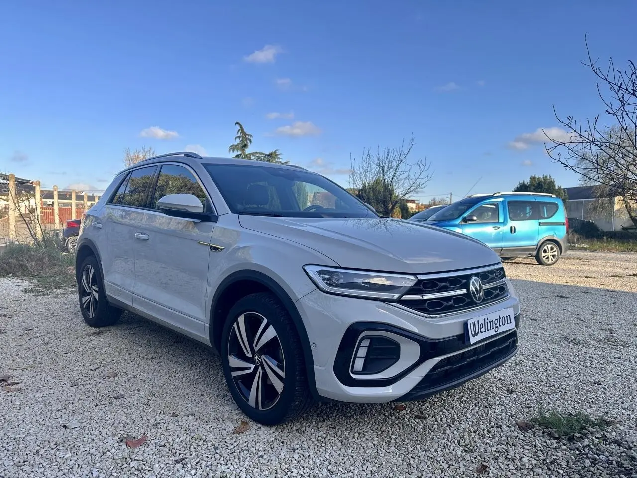 Volkswagen T-Roc gris en 3/4 avant droit, avec jantes R-Line et calandre noire distinctive.