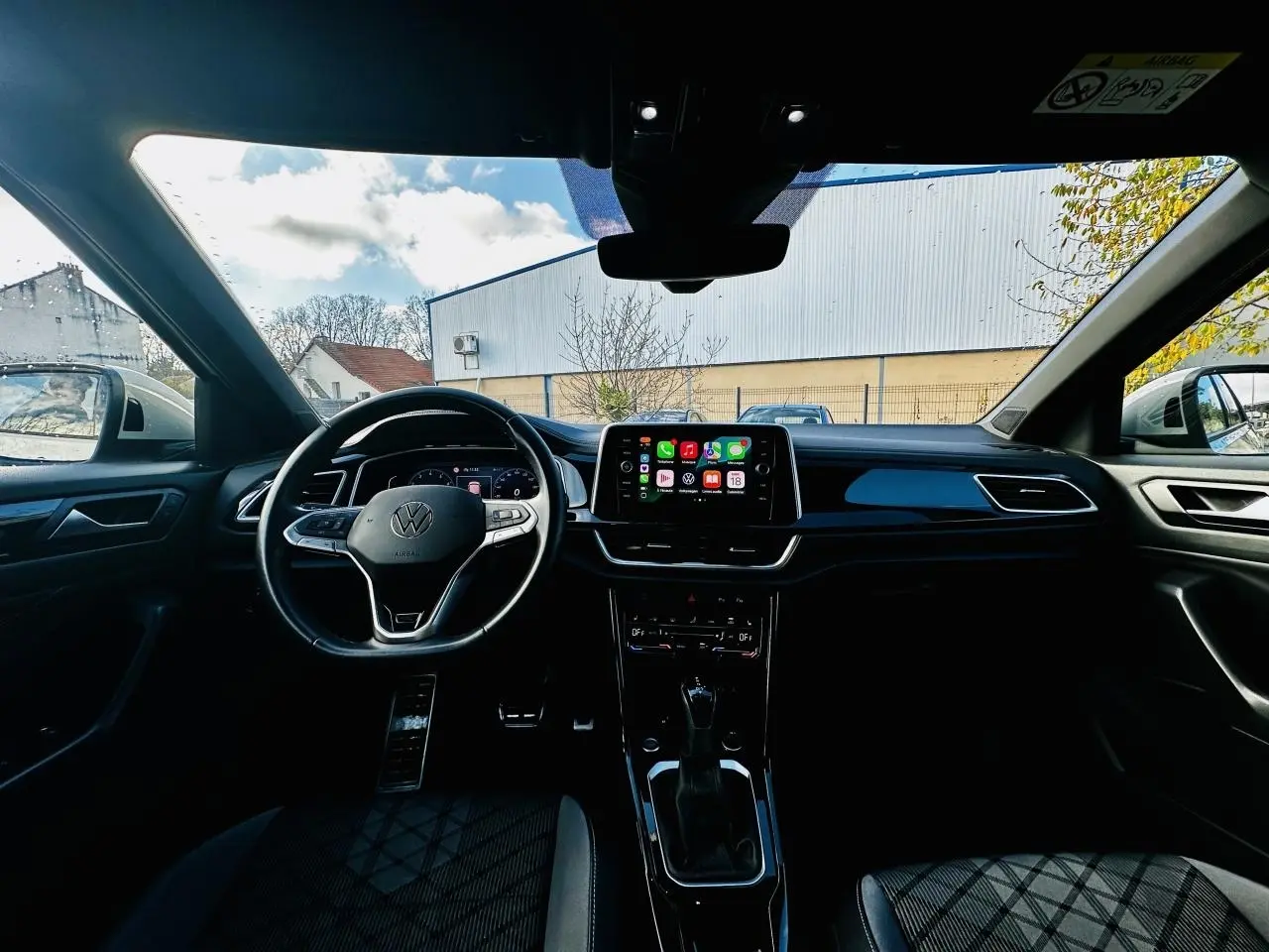 Intérieur du Volkswagen T-Roc gris 2024 vu de face, avec volant multifonction et écran tactile central allumé.