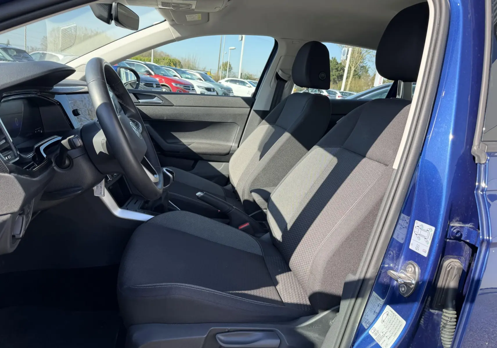 Vue intérieure côté conducteur du Volkswagen Taigo bleu 2025, montrant les sièges avant et le volant multifonction cuir.