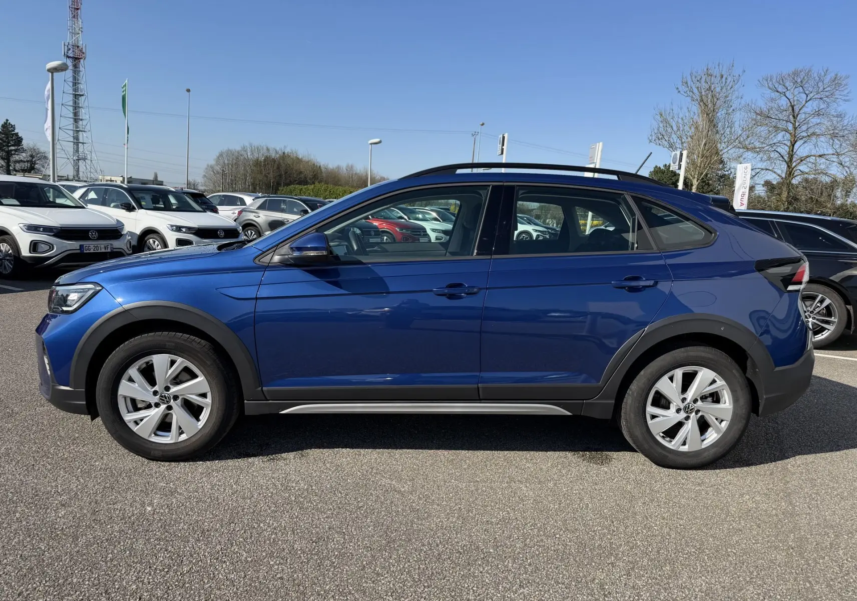 Vue de profil côté gauche d'un Volkswagen Taigo bleu métallisé avec jantes alliage et barres de toit noires.