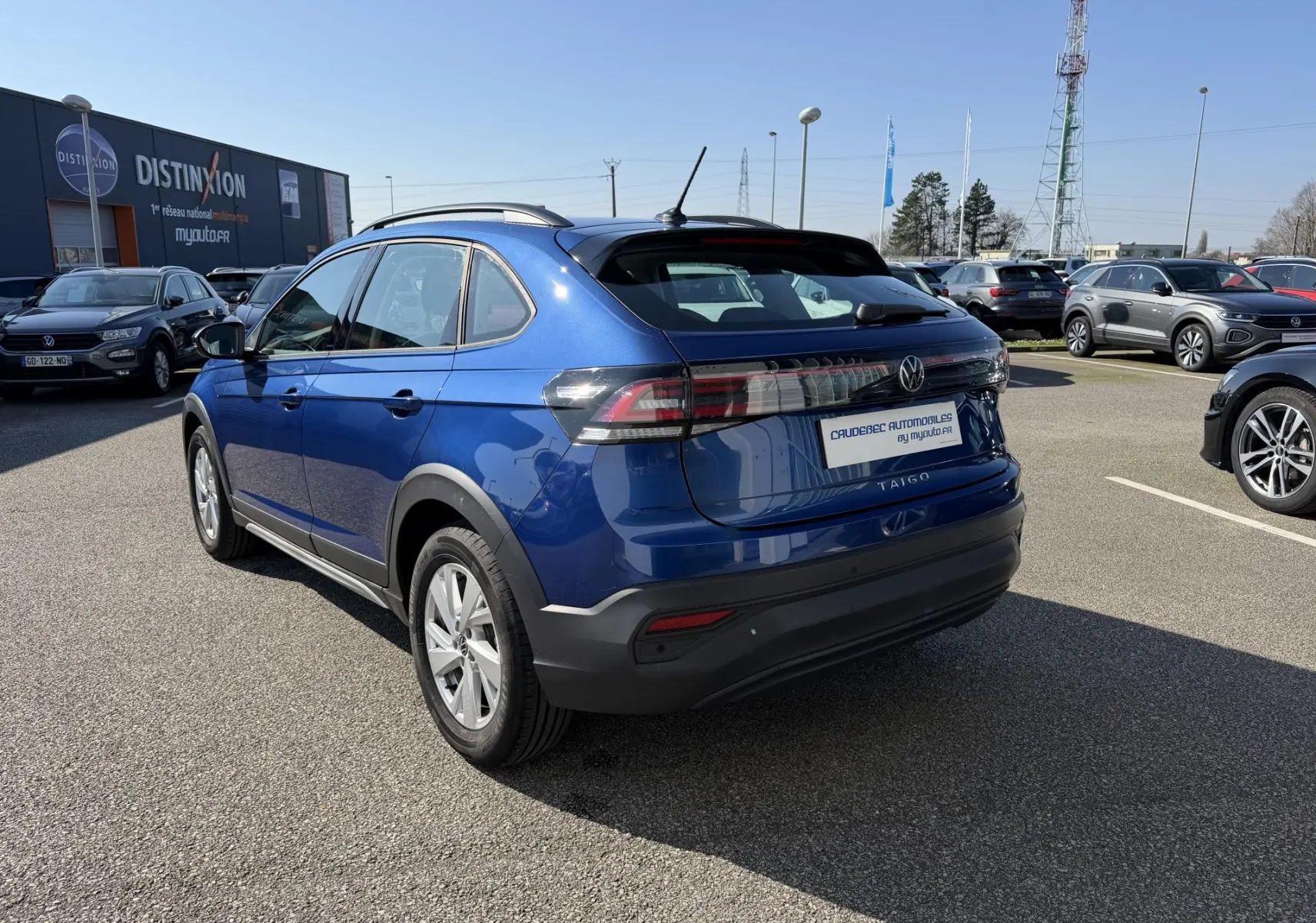 Vue 3/4 arrière droite d'un Volkswagen Taigo bleu métallisé avec barres de toit et feux arrière LED.