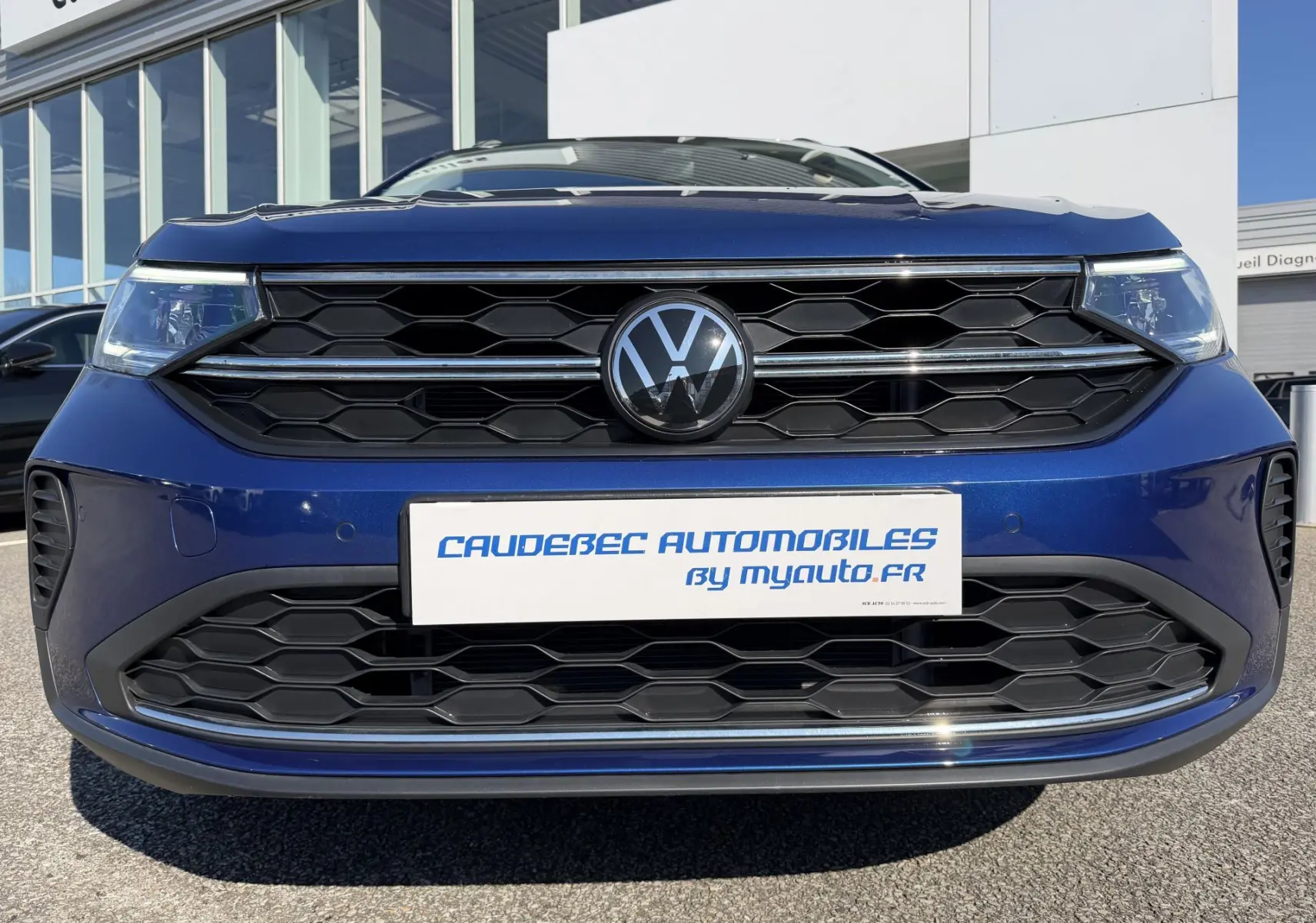 Vue frontale rapprochée du Volkswagen Taigo 2025 en bleu métallisé avec calandre noire et logo VW central.