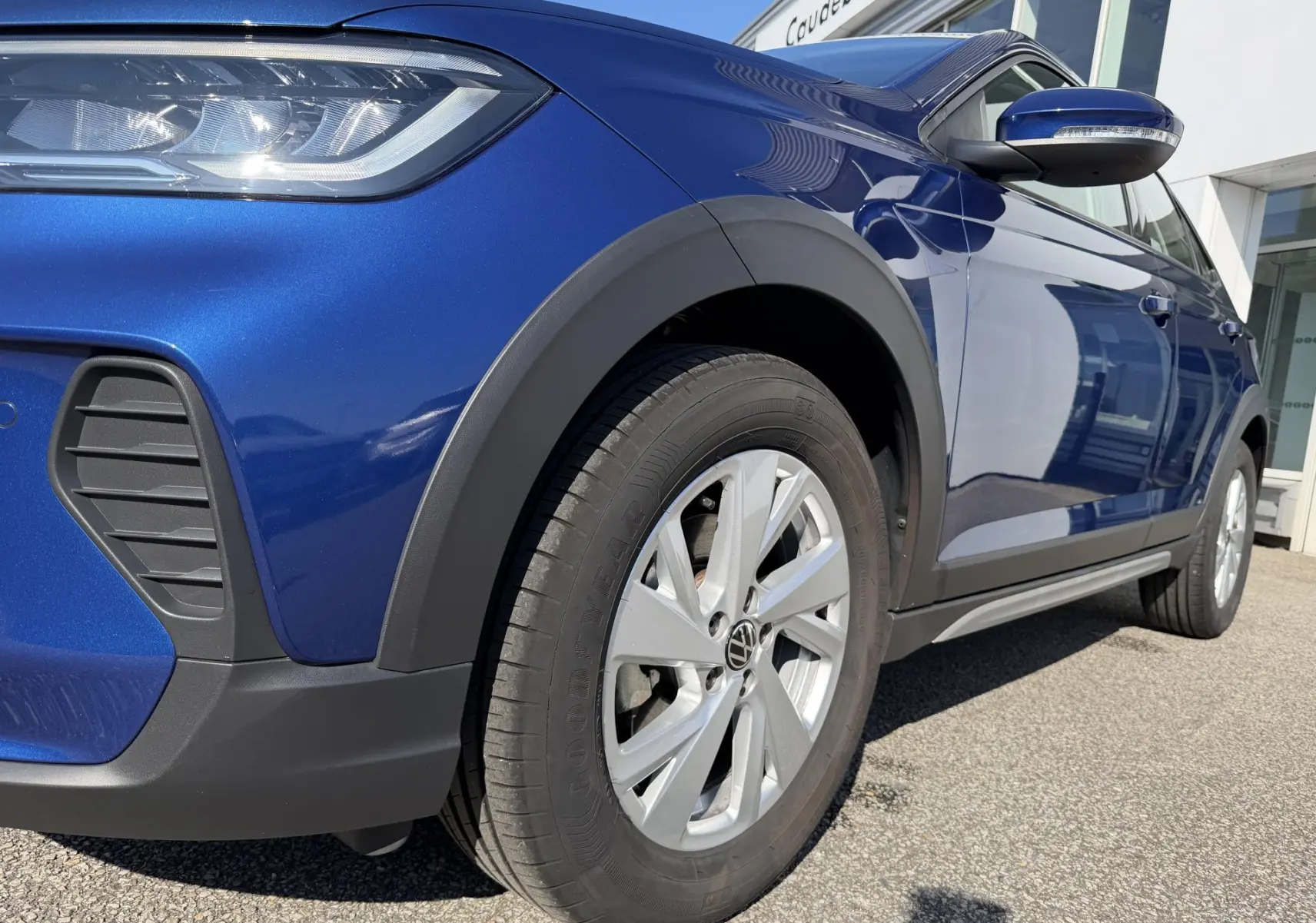 Vue 3/4 avant droit du Volkswagen Taigo bleu métallisé avec jantes alliage et protections plastiques noires.