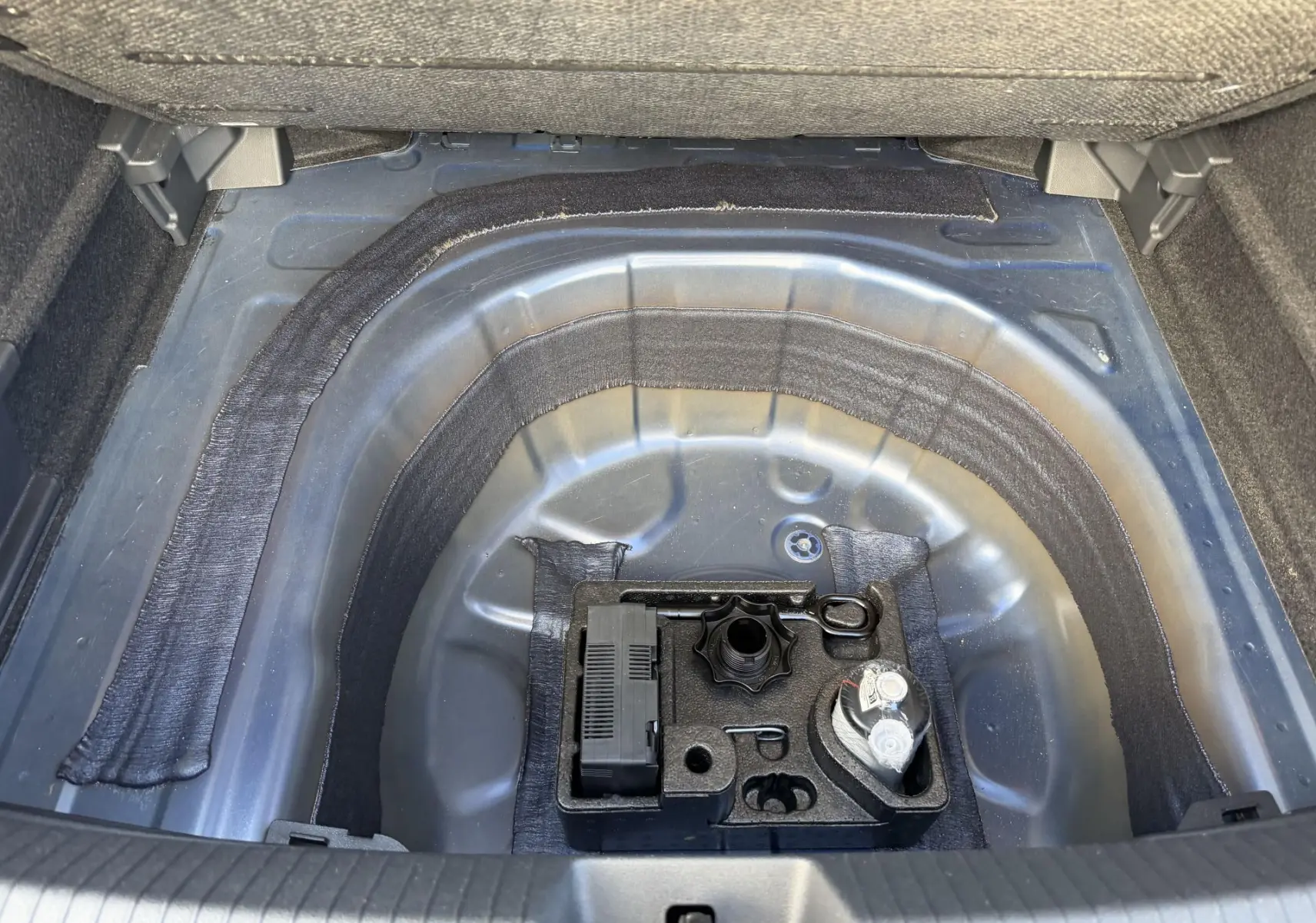 Vue plongeante sur le coffre ouvert d’un Volkswagen Taigo bleu, montrant le compartiment à outils et kit de dépannage.