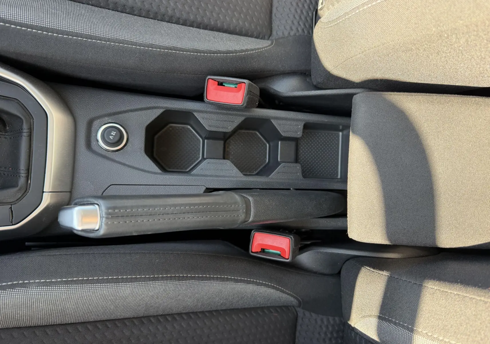 Vue plongeante sur la console centrale noire du Volkswagen Taigo 2025 avec frein à main manuel et porte-gobelets.