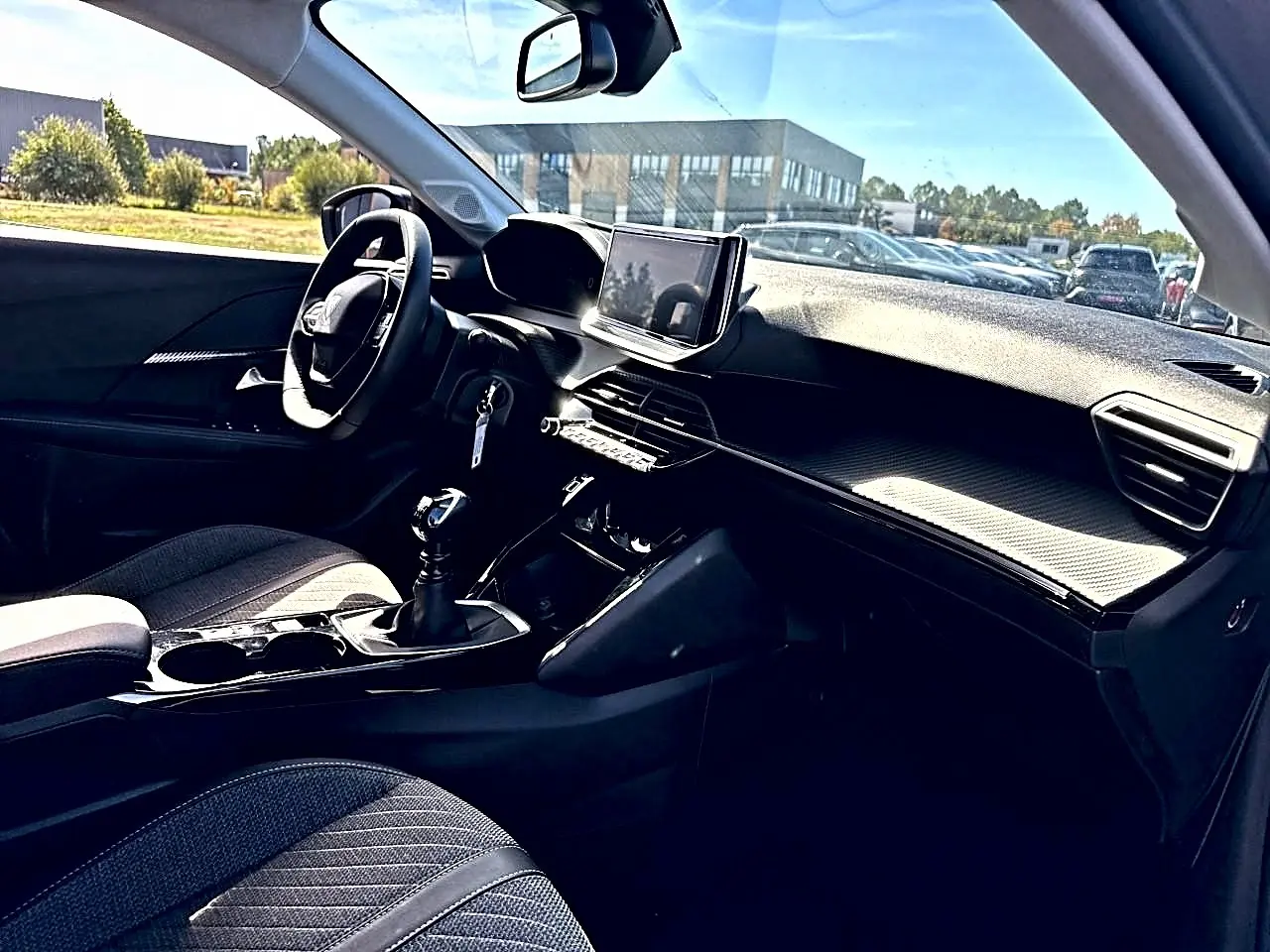 Vue intérieure côté conducteur de la Peugeot 208 1.2 100 Allure avec tableau de bord noir et écran tactile central.