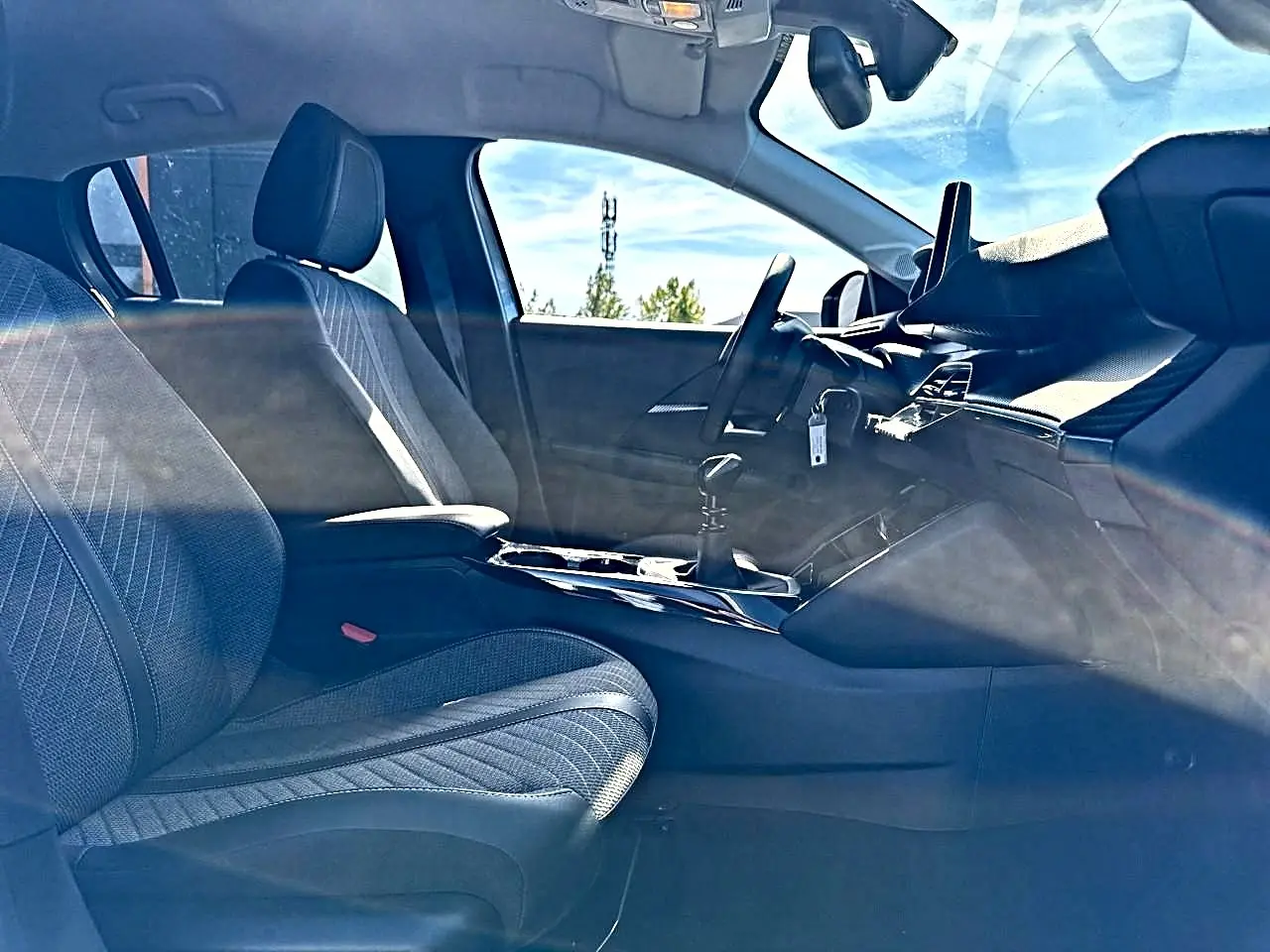 Vue intérieure côté conducteur de la Peugeot 208 1.2 100 allure avec sièges tissu gris et tableau de bord moderne.