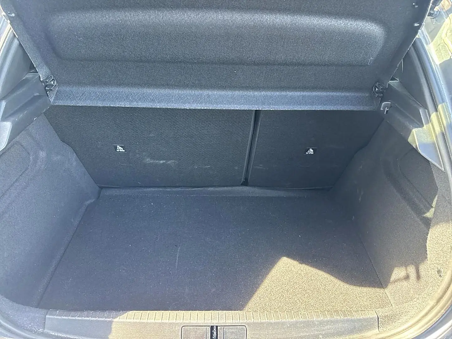 Coffre ouvert de la Peugeot 208 1.2 100 allure gris artense, montrant l'espace de chargement vide et les dossiers de banquette rabattables.