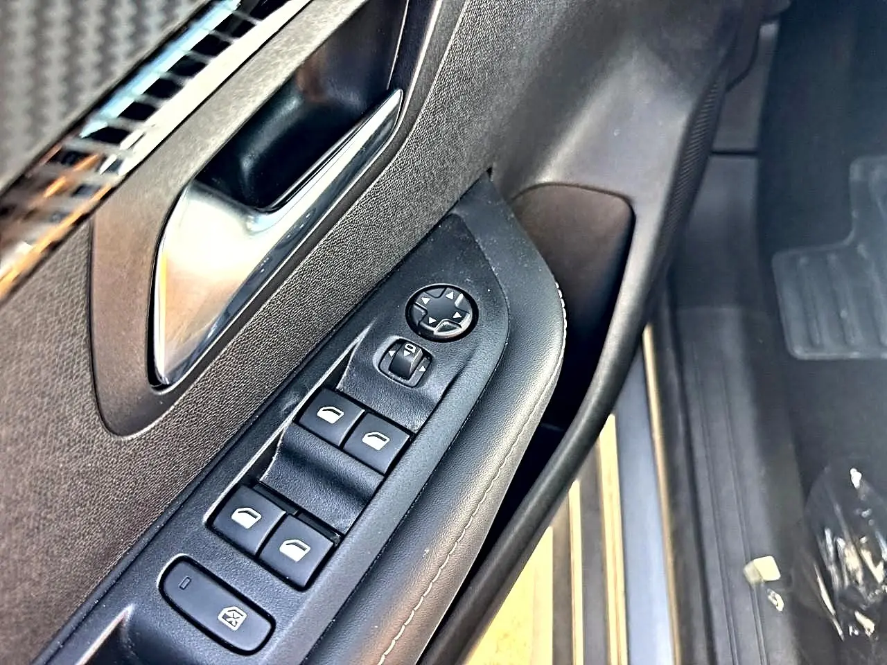 Gros plan sur la commande des vitres électriques côté gauche de la porte avant d'une Peugeot 208 gris Artense.