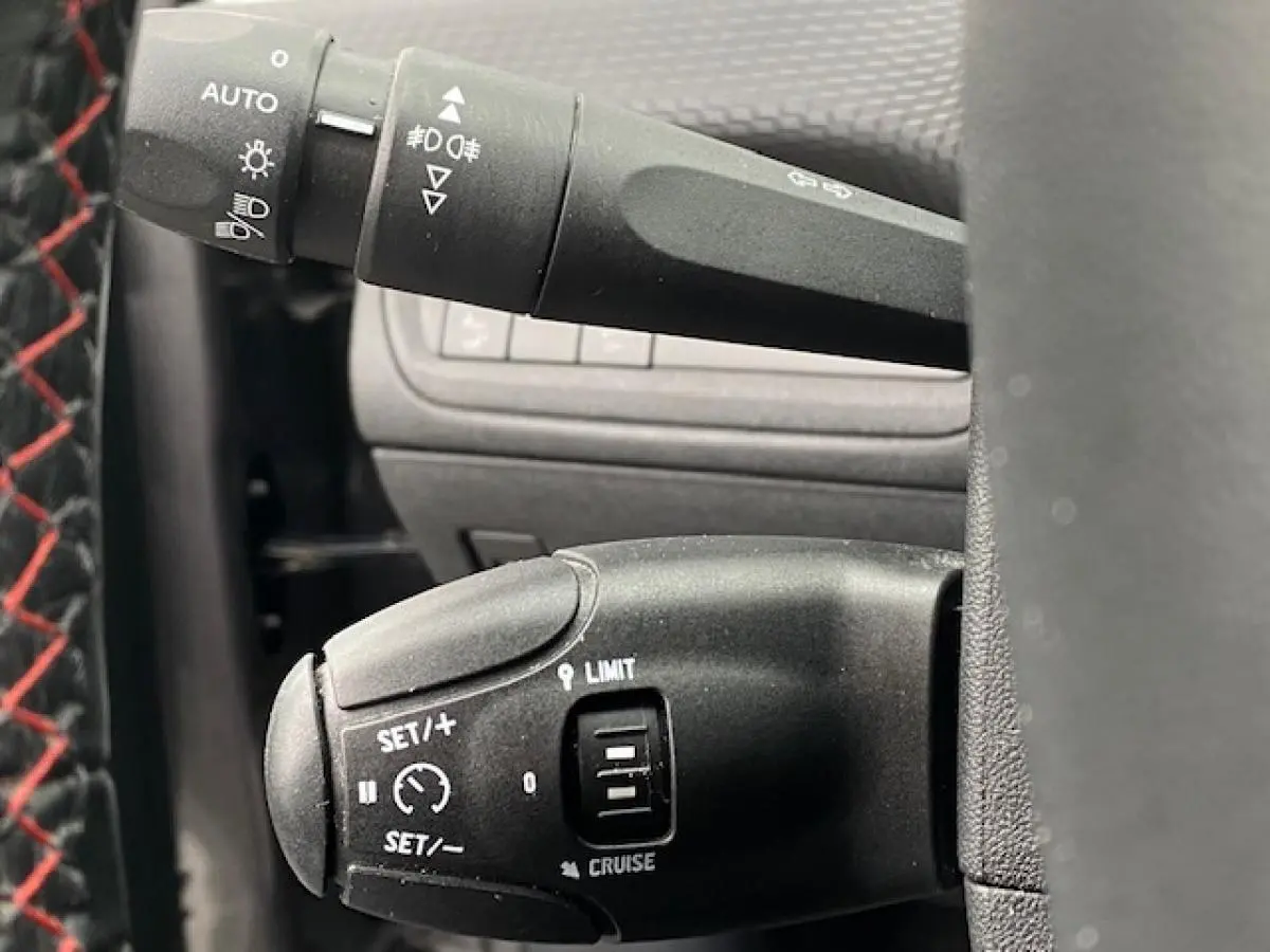 Gros plan sur la commande de régulateur de vitesse du Peugeot 2008 gris foncé, avec volant en cuir noir et surpiqûres rouges.