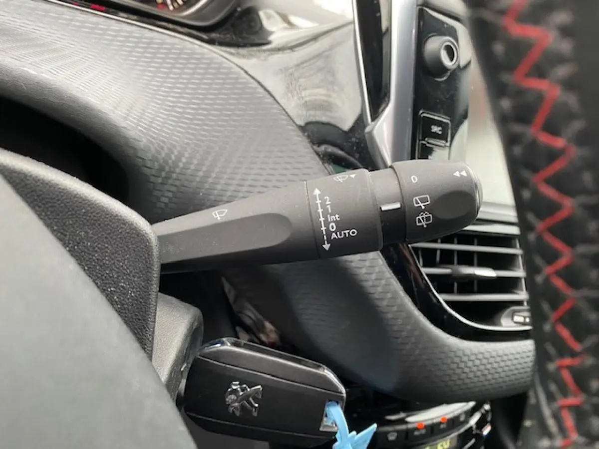 Gros plan sur la commande d’essuie-glace et la clé Peugeot dans l’habitacle noir du 2008 gris foncé.