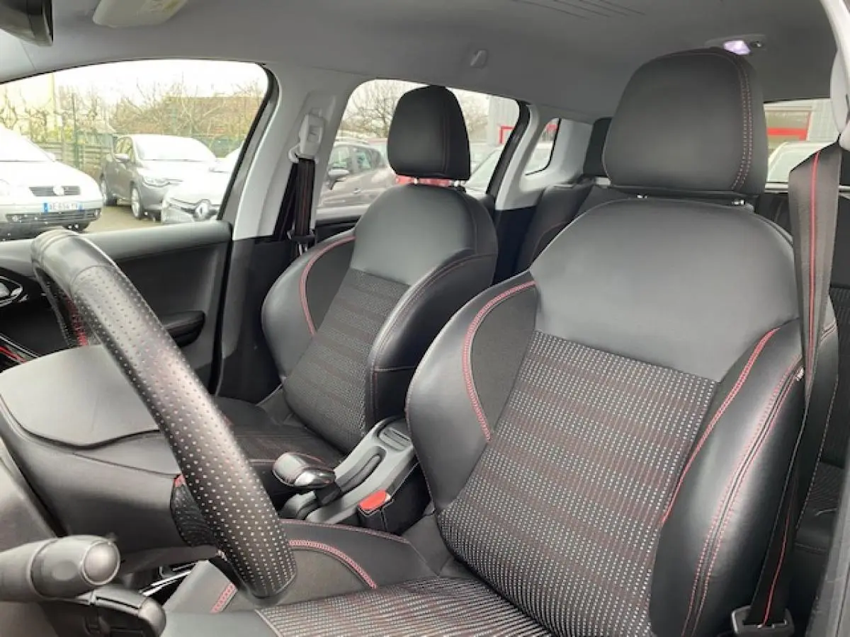 Intérieur de la Peugeot 2008 gris foncé, vue sur les sièges avant en cuir noir avec surpiqûres rouges et volant perforé.