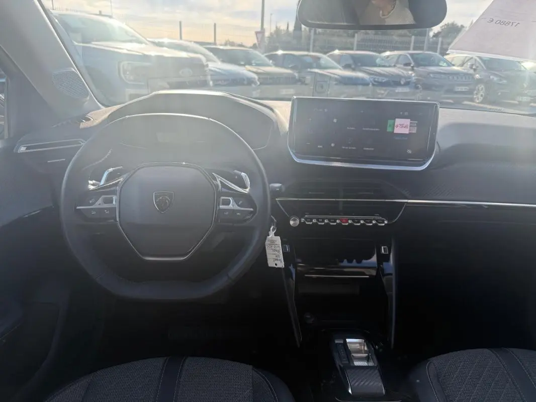 Vue intérieure de face du poste de conduite de la Peugeot 208 Hybrid 110 e-DCS6 Allure 2024 avec écran tactile et volant compact noir.