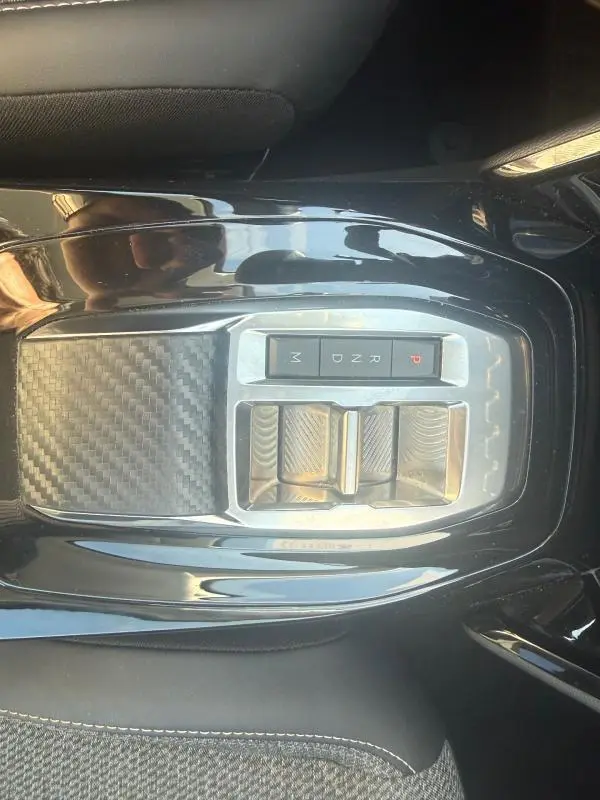 Vue rapprochée de la console centrale noire brillante du Peugeot 208 Hybrid 110 e-DCS6 Allure 2024 avec sélecteur de vitesses automatique.