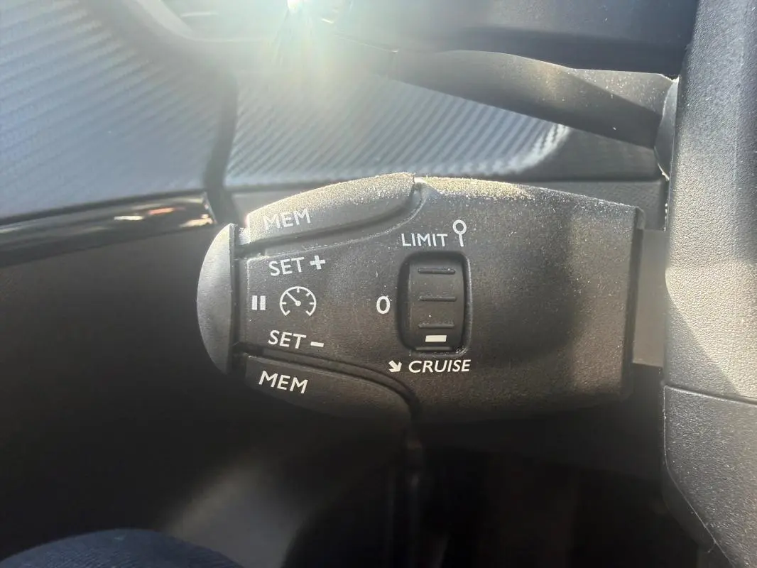 Gros plan sur la commande de régulateur de vitesse du Peugeot 208 Hybrid blanc, côté gauche du volant.