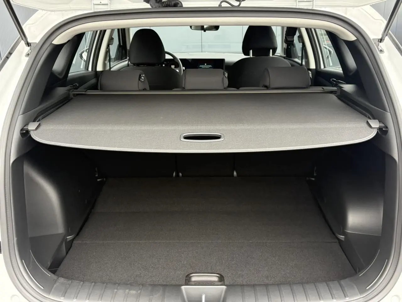 Vue arrière du coffre ouvert du Hyundai Tucson blanc Serenity, avec cache-bagages déployé et intérieur noir.