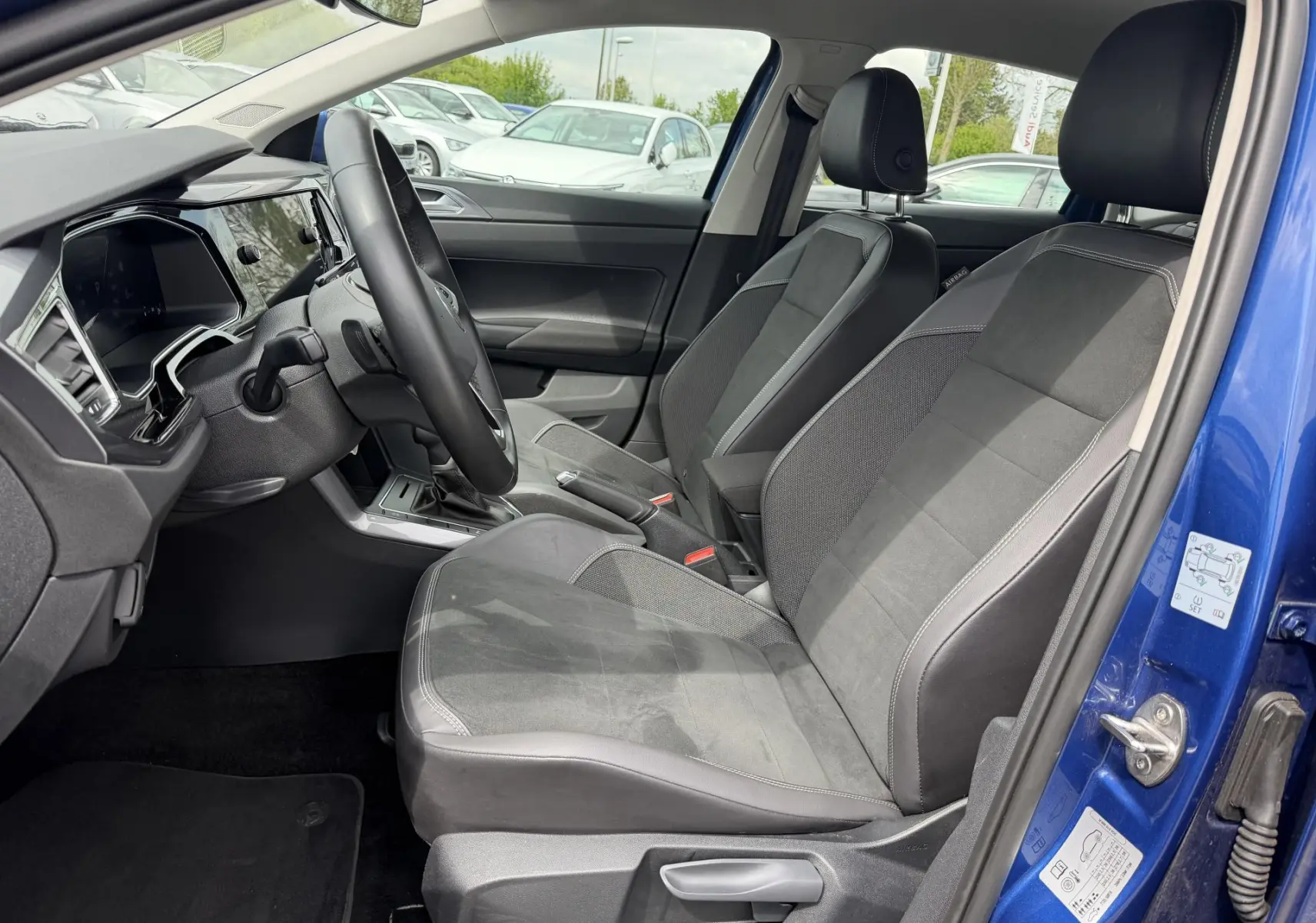 Vue intérieure côté conducteur de la Volkswagen Polo bleue 2025, sièges sport noirs et volant cuir multifonctions.