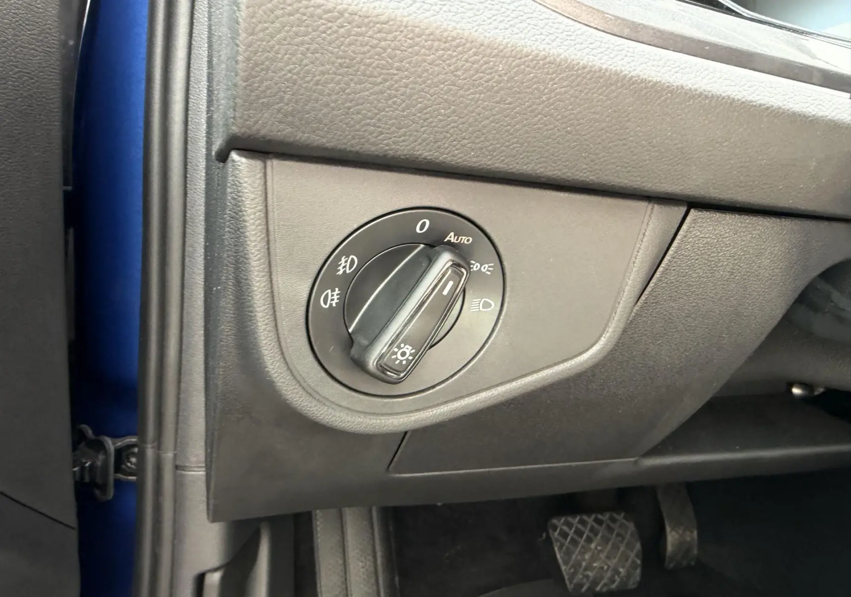 Détail du bouton de commande des feux sur le côté gauche du tableau de bord d'une Volkswagen Polo bleue 2025.
