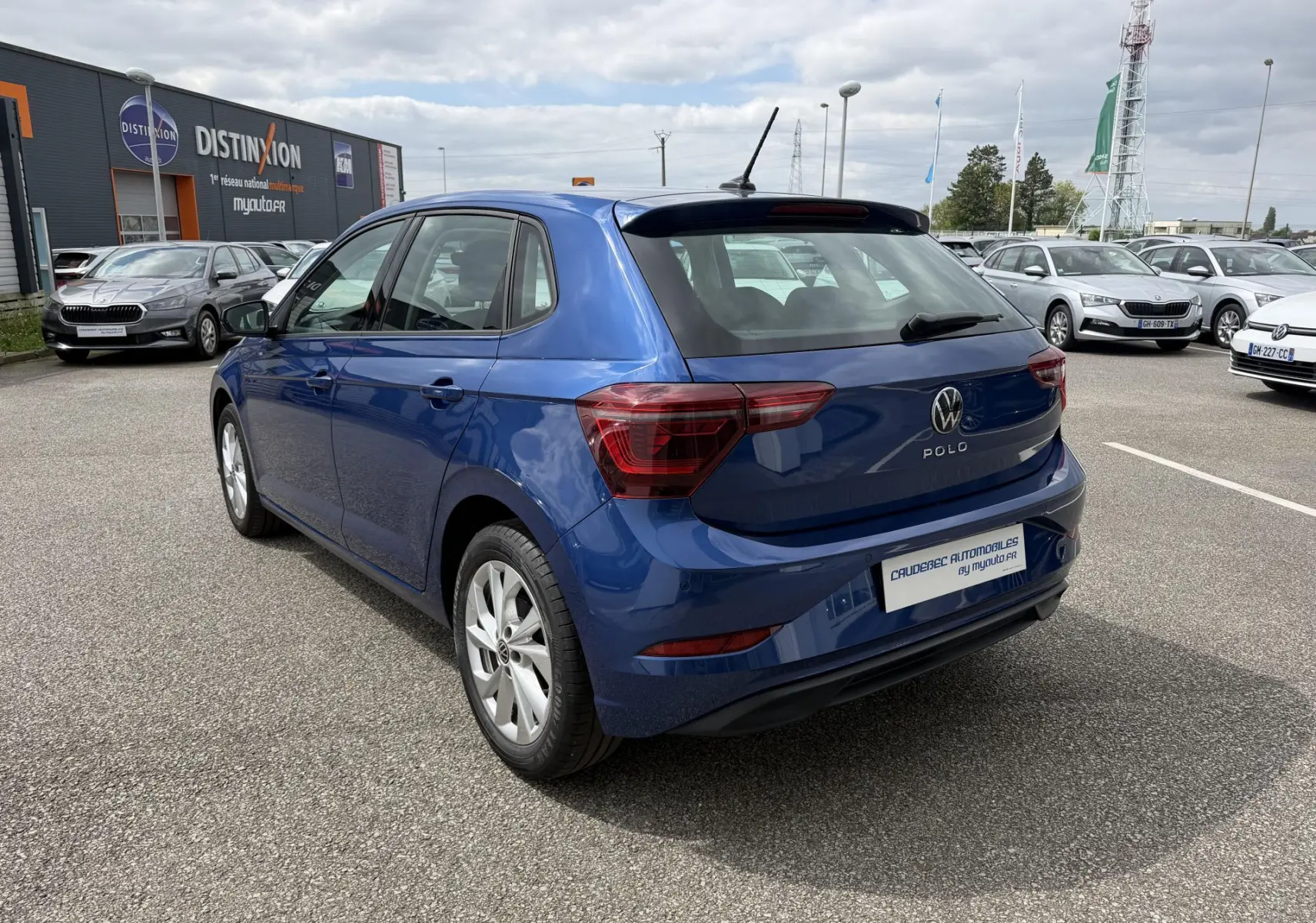 Vue 3/4 arrière droite d'une Volkswagen Polo bleue métallisée garée en extérieur sur un parking de concession.