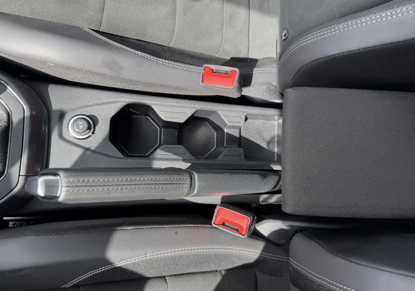 Vue plongeante sur la console centrale noire de la Volkswagen Polo avec frein à main cuir et porte-gobelets.