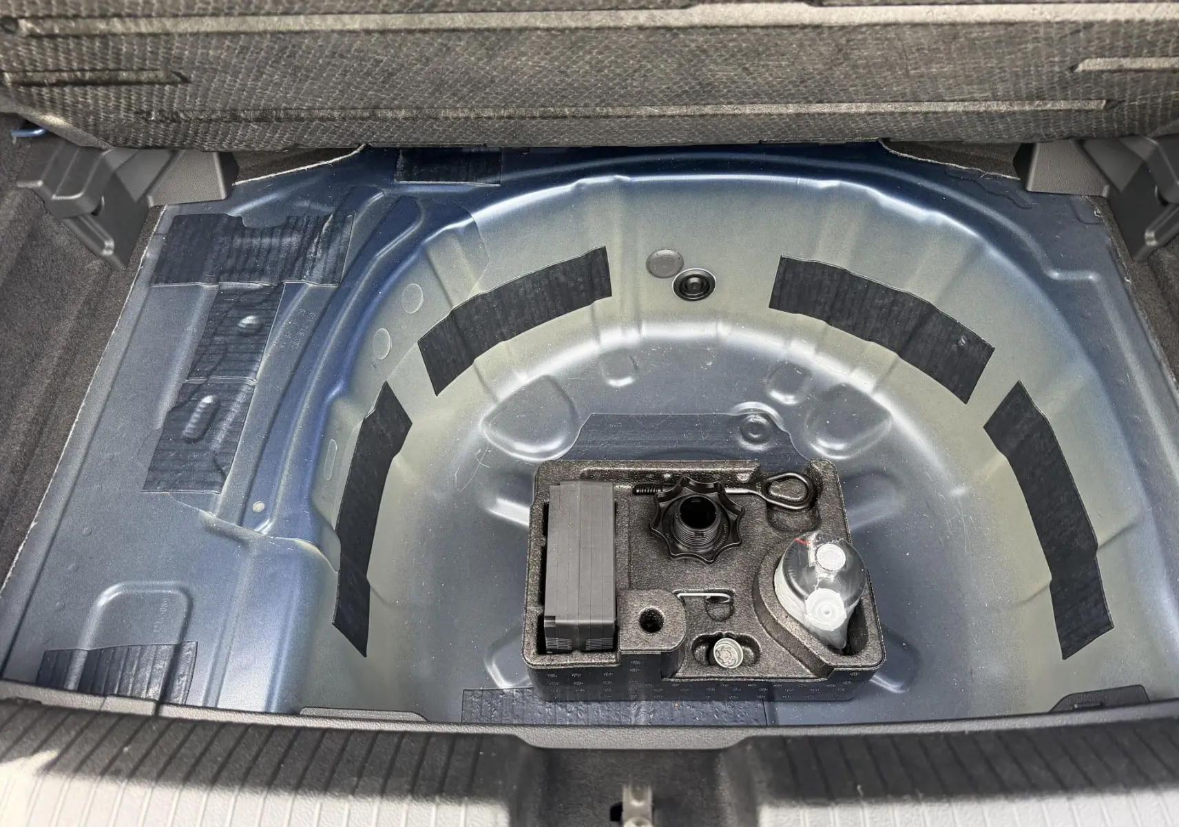 Vue plongeante sur le coffre ouvert d'une Volkswagen Polo bleue 2025, montrant le rangement sous plancher métallique.