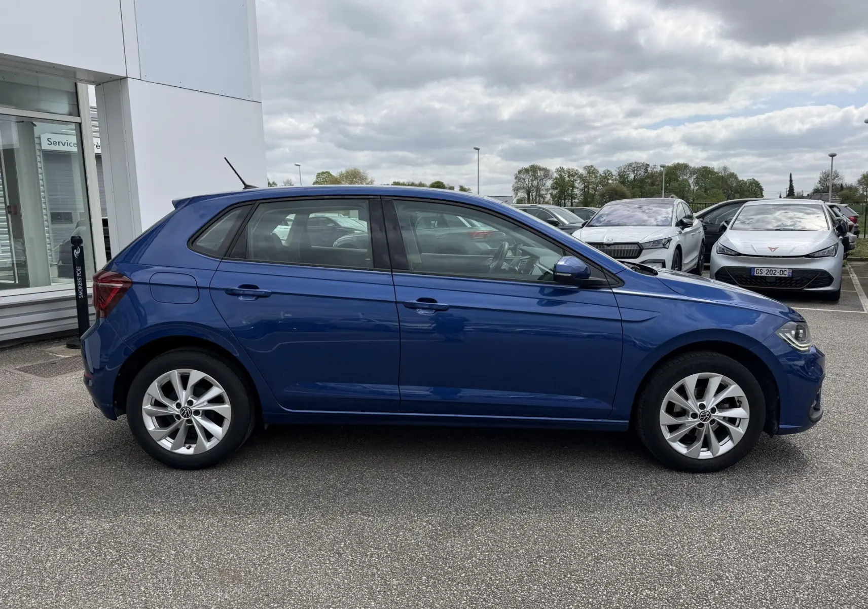 Vue latérale gauche d'une Volkswagen Polo bleue métallisée avec jantes alliage 16 pouces, stationnée sur un parking.