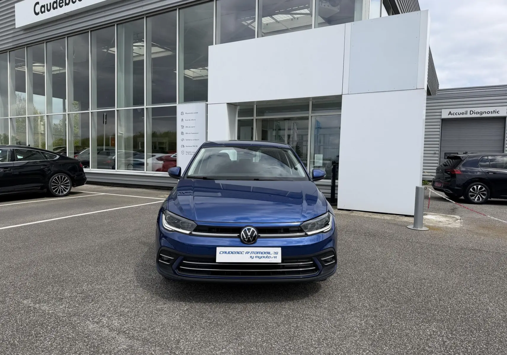 Vue de face d'une Volkswagen Polo bleue métallisée stationnée devant un showroom avec calandre et phares LED visibles.