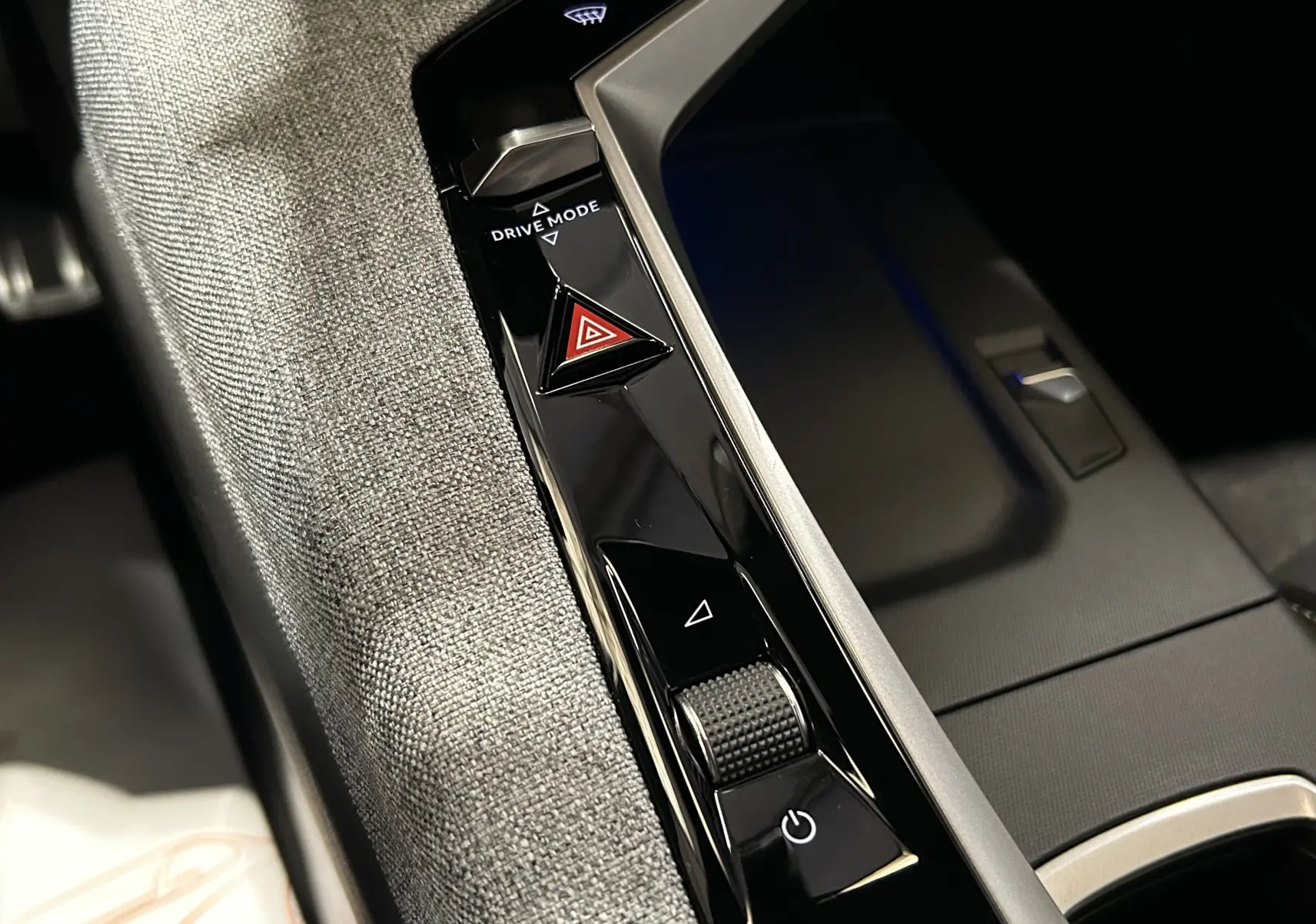 Gros plan sur la console centrale noire et grise du Peugeot 3008 Hybrid 2025, avec bouton Drive Mode et signal d’alerte.