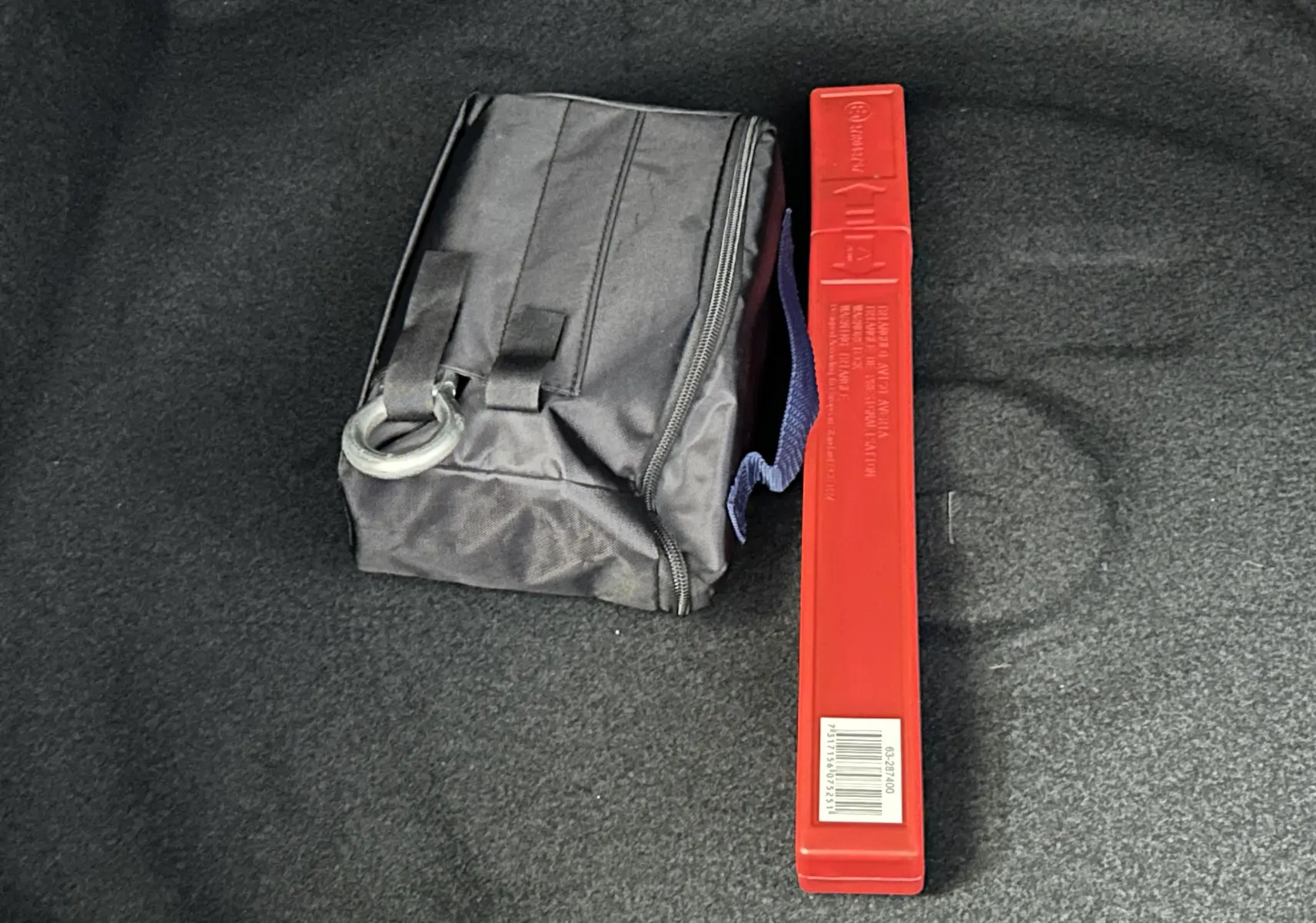 Coffret de secours noir et triangle de signalisation rouge posés sur le tapis de coffre d’un véhicule.