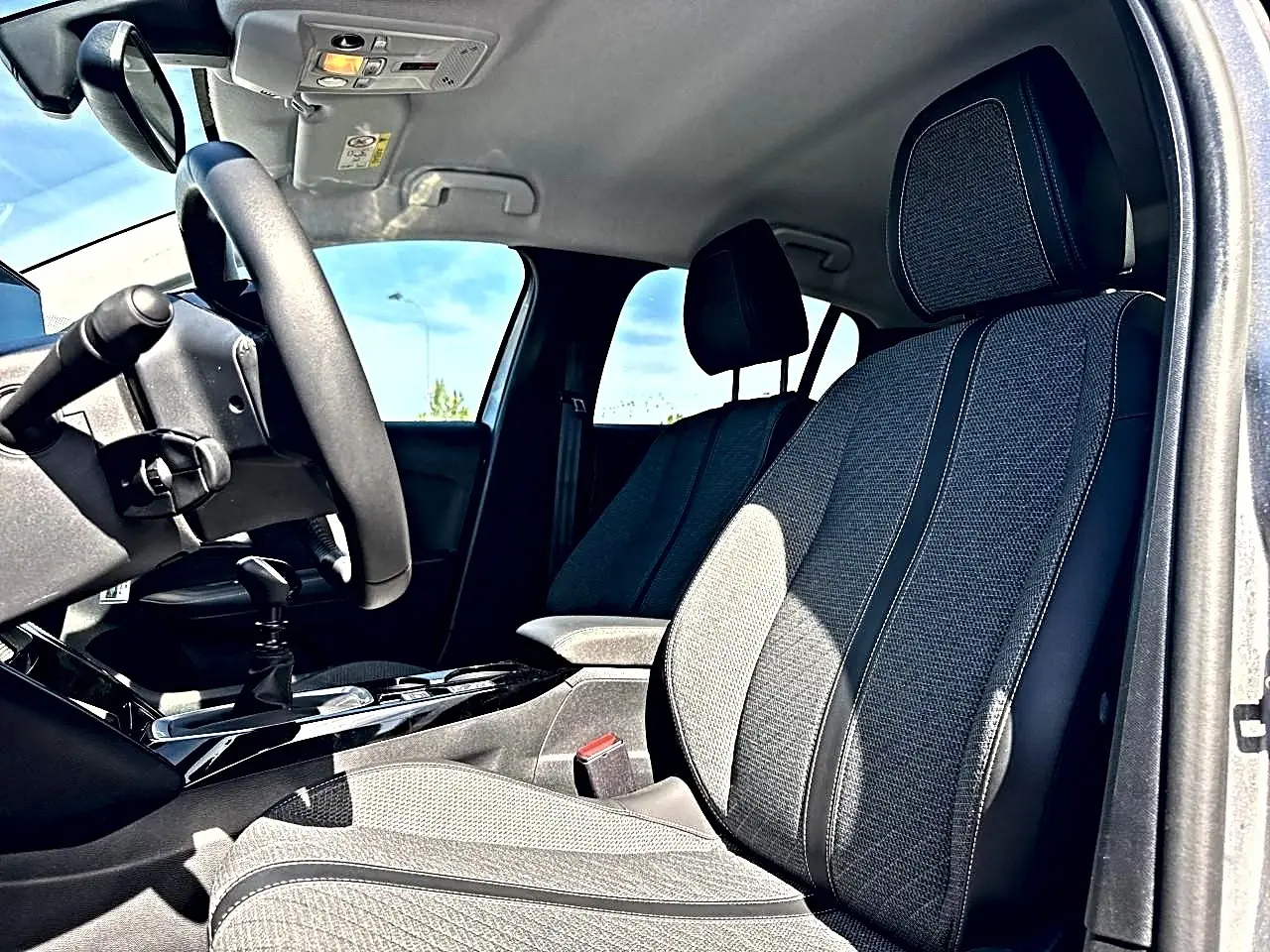 Vue intérieure côté conducteur de la Peugeot 208 1.2 100 Allure avec sièges tissu gris et volant noir.