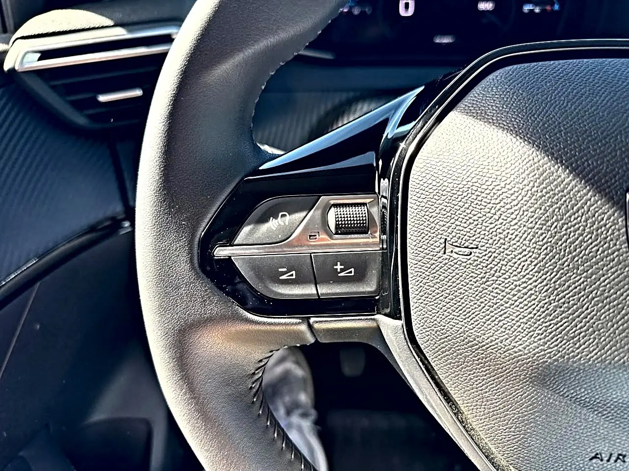 Gros plan sur le volant noir de la Peugeot 208 1.2 100 Allure, montrant les commandes audio et téléphone à gauche.