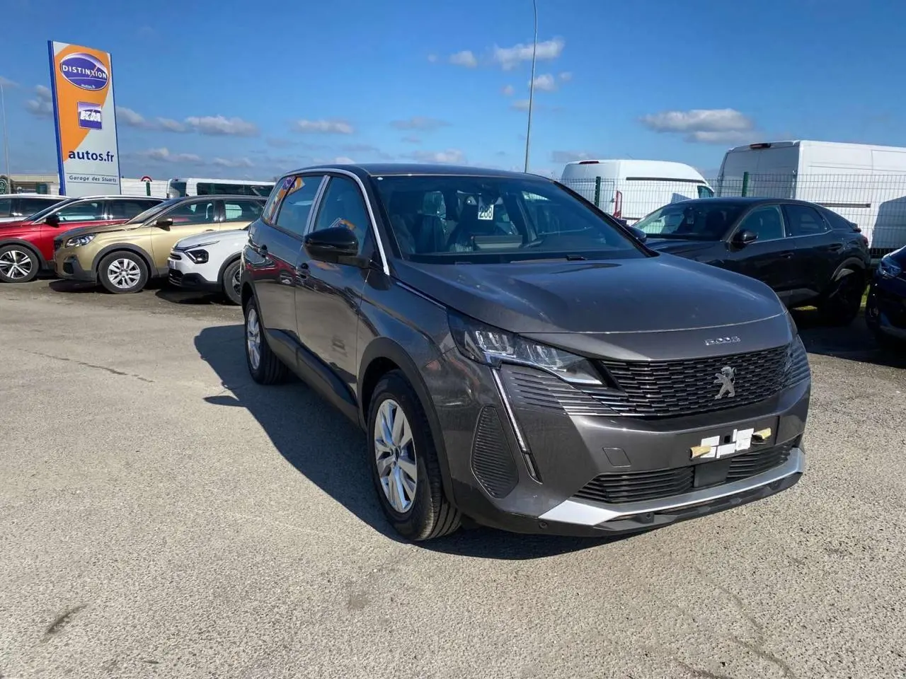 Peugeot 5008 gris platinium métal vue 3/4 avant droit sur parking avec calandre noire et phares LED.