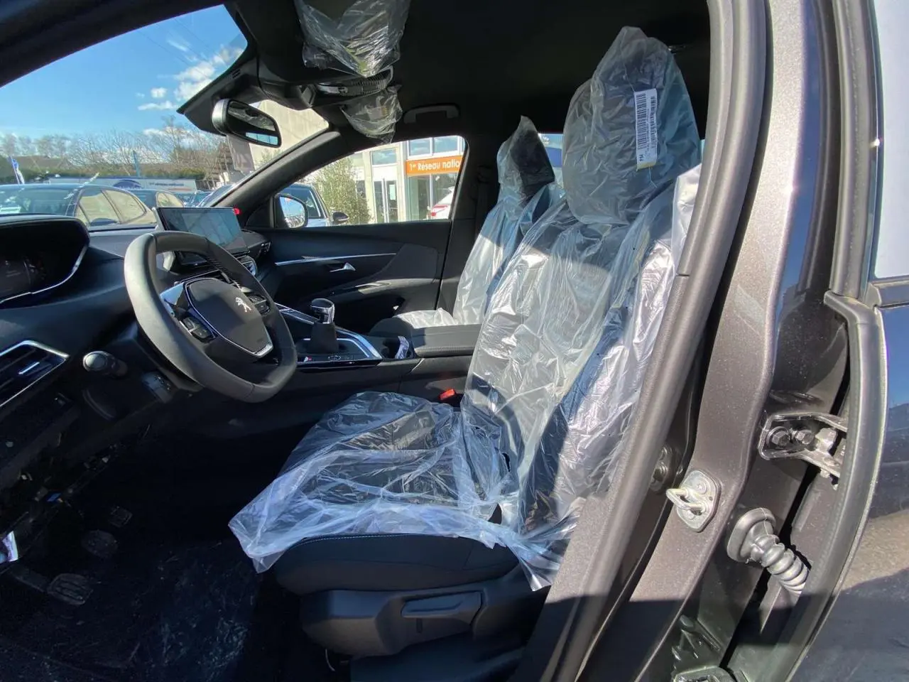 Intérieur avant droit du Peugeot 5008 gris platinium 2023 avec sièges protégés par film plastique.