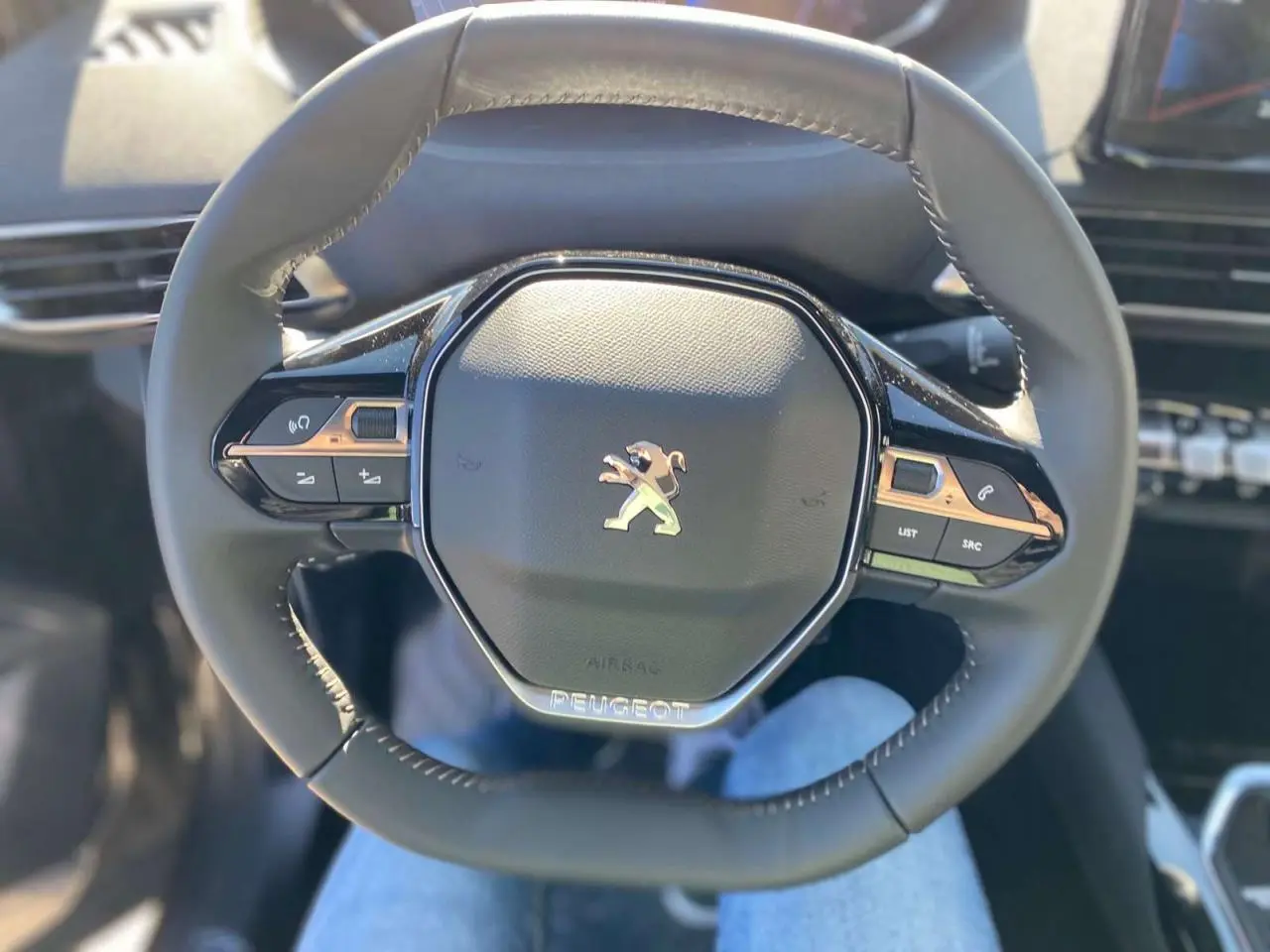 Vue rapprochée du volant compact multifonctions du Peugeot 5008 2023 avec logo lion chromé au centre.